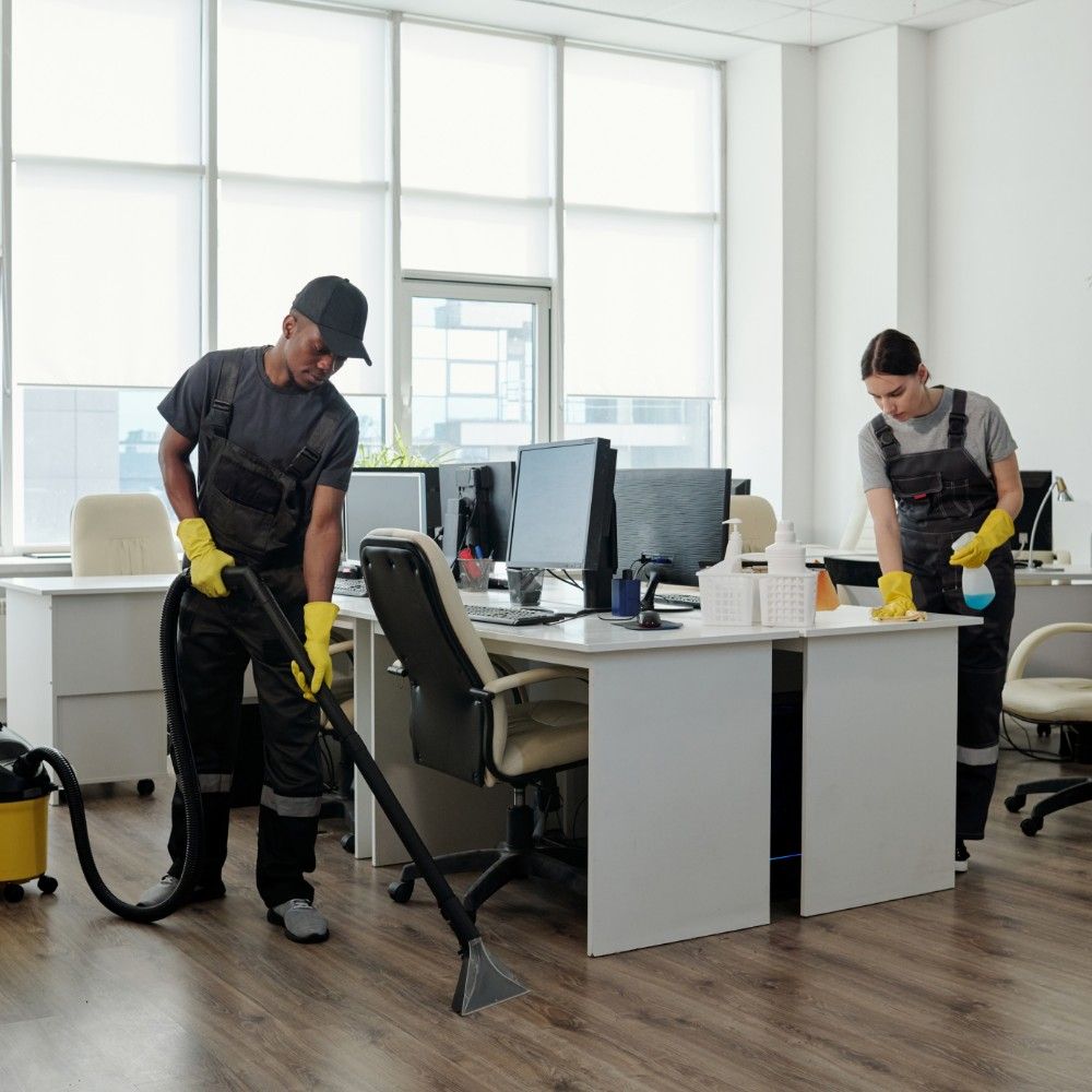 Two cleaners in uniforms cleaning a bright open-plan office